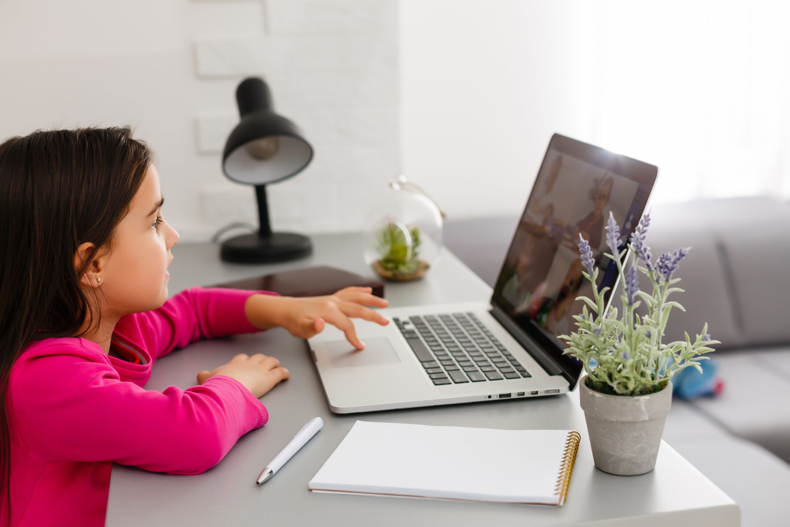 A young girl using a laptop displaying a video call with other children
