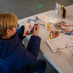 A volunteer pointing at a laptop that is connected to different pieces of fruit using some wires