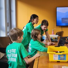 Four children wearing t-shirts that read 'Plastic Pollution Solution' looking at a laptop surrounded by LEGO