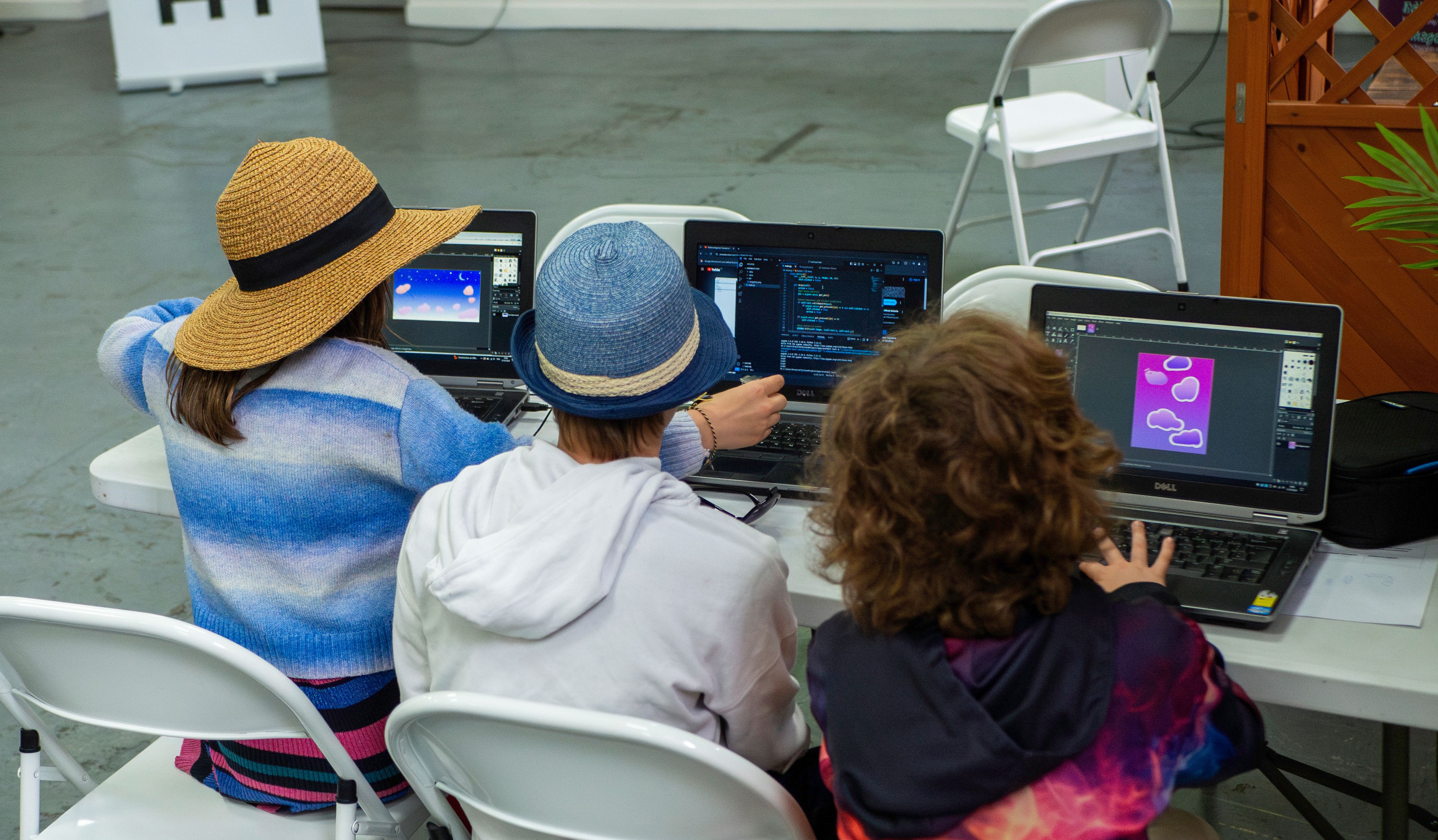 Three Prewired attendees, sitting next to each other, working on laptops with code and graphics editors