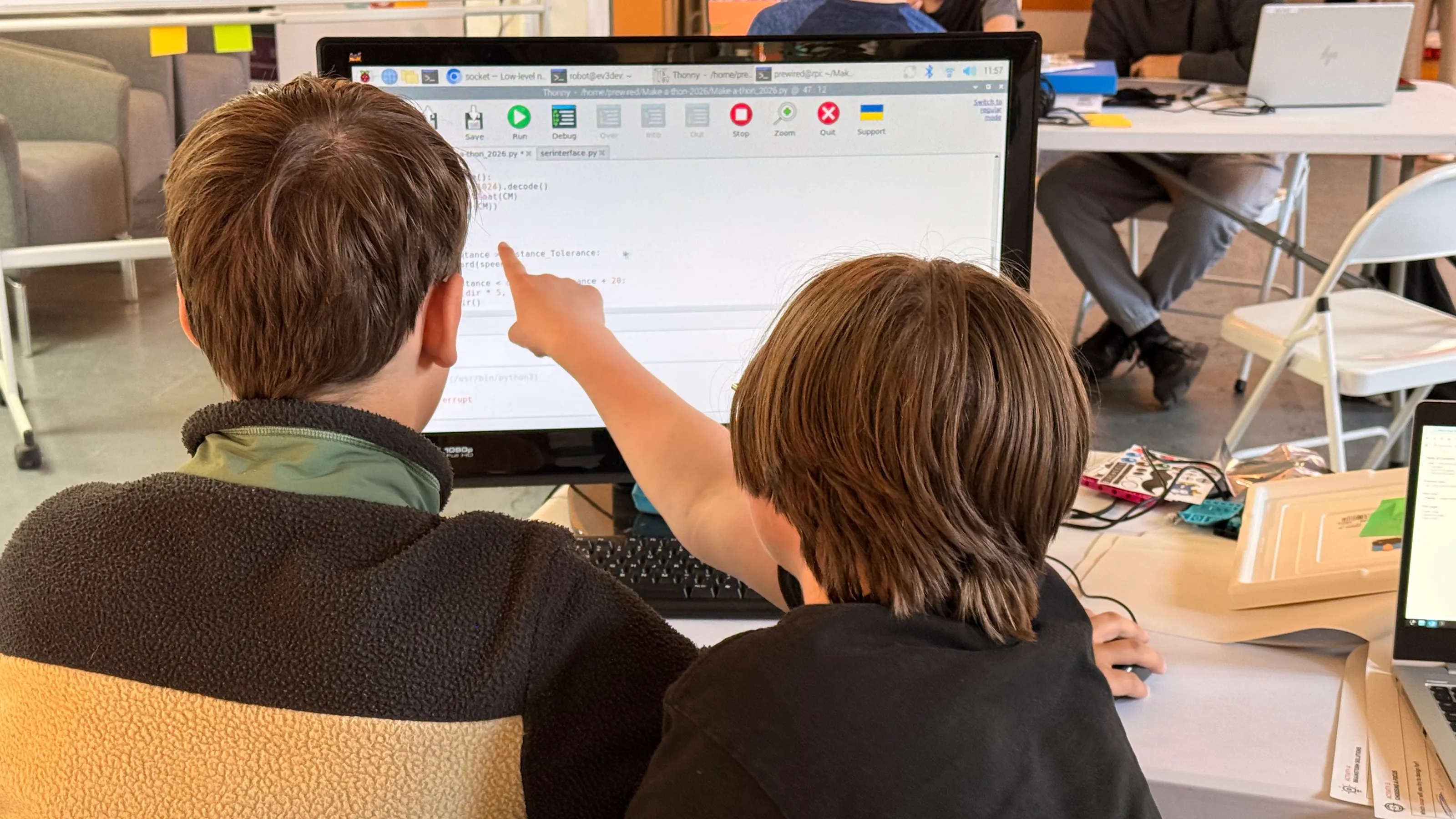 Two young people looking at a code editor on a display, with one of them pointing to a line of code