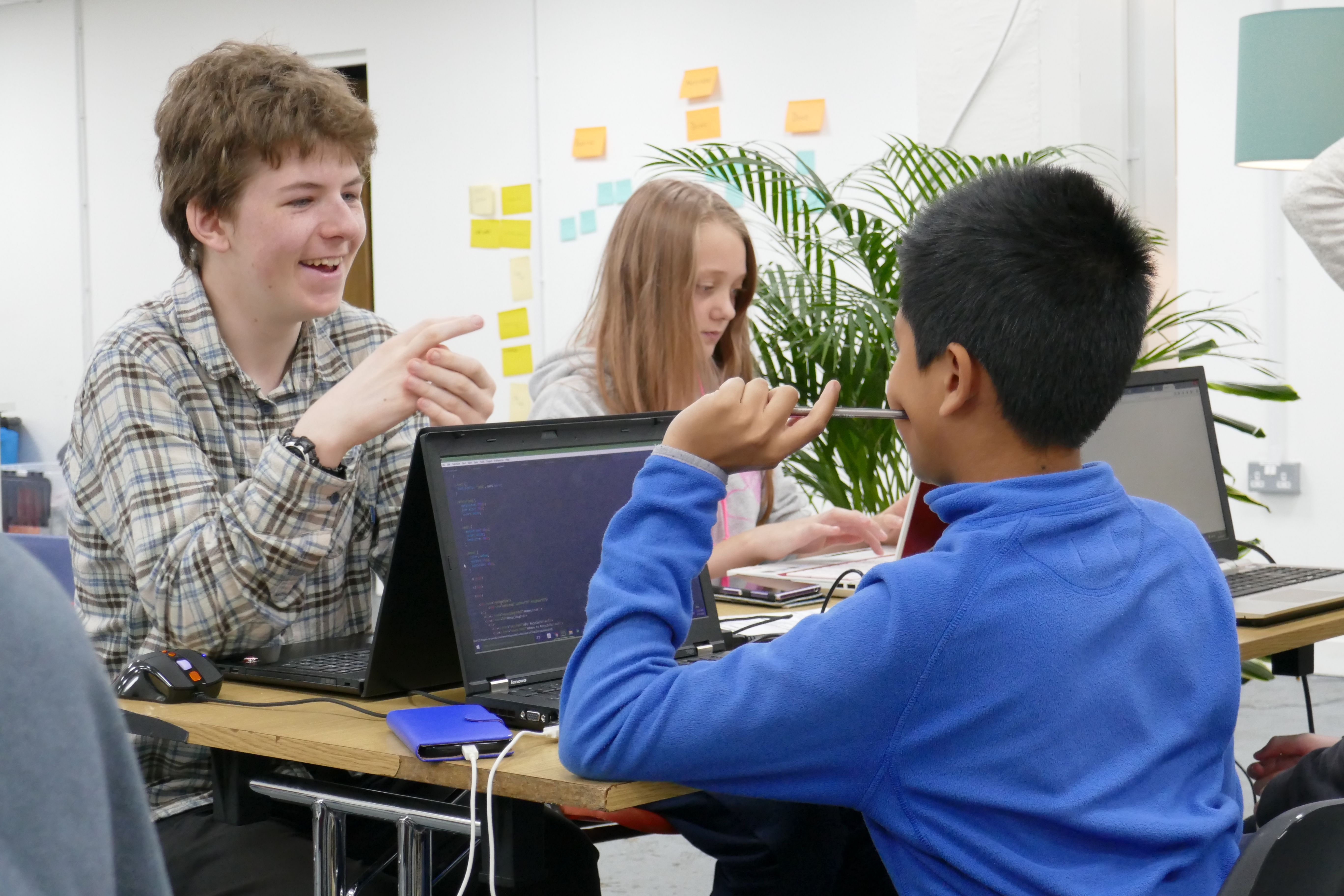 Three teenagers coding on laptops while chatting to each other
