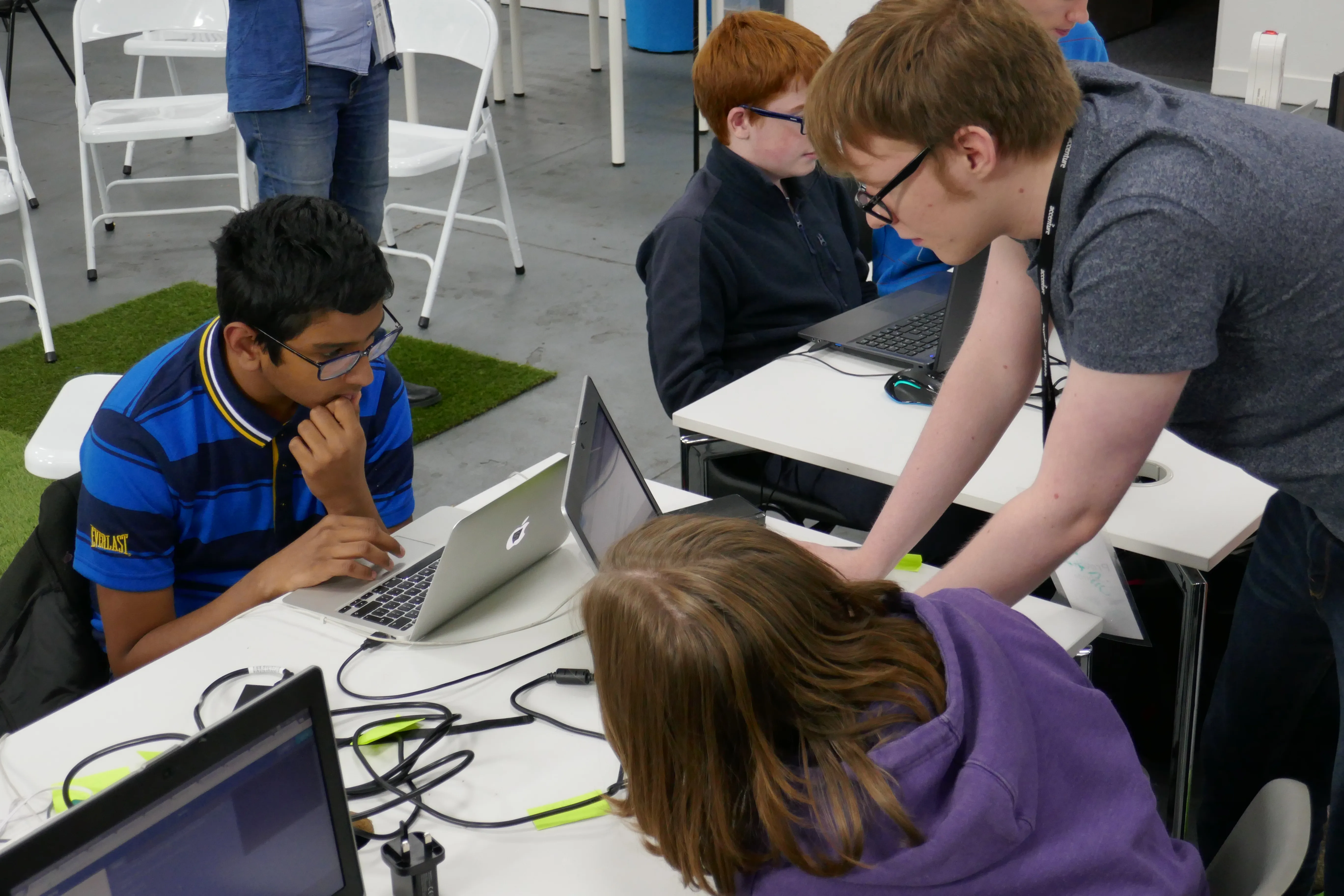 Two young people and an adult mentor around a table looking at laptops