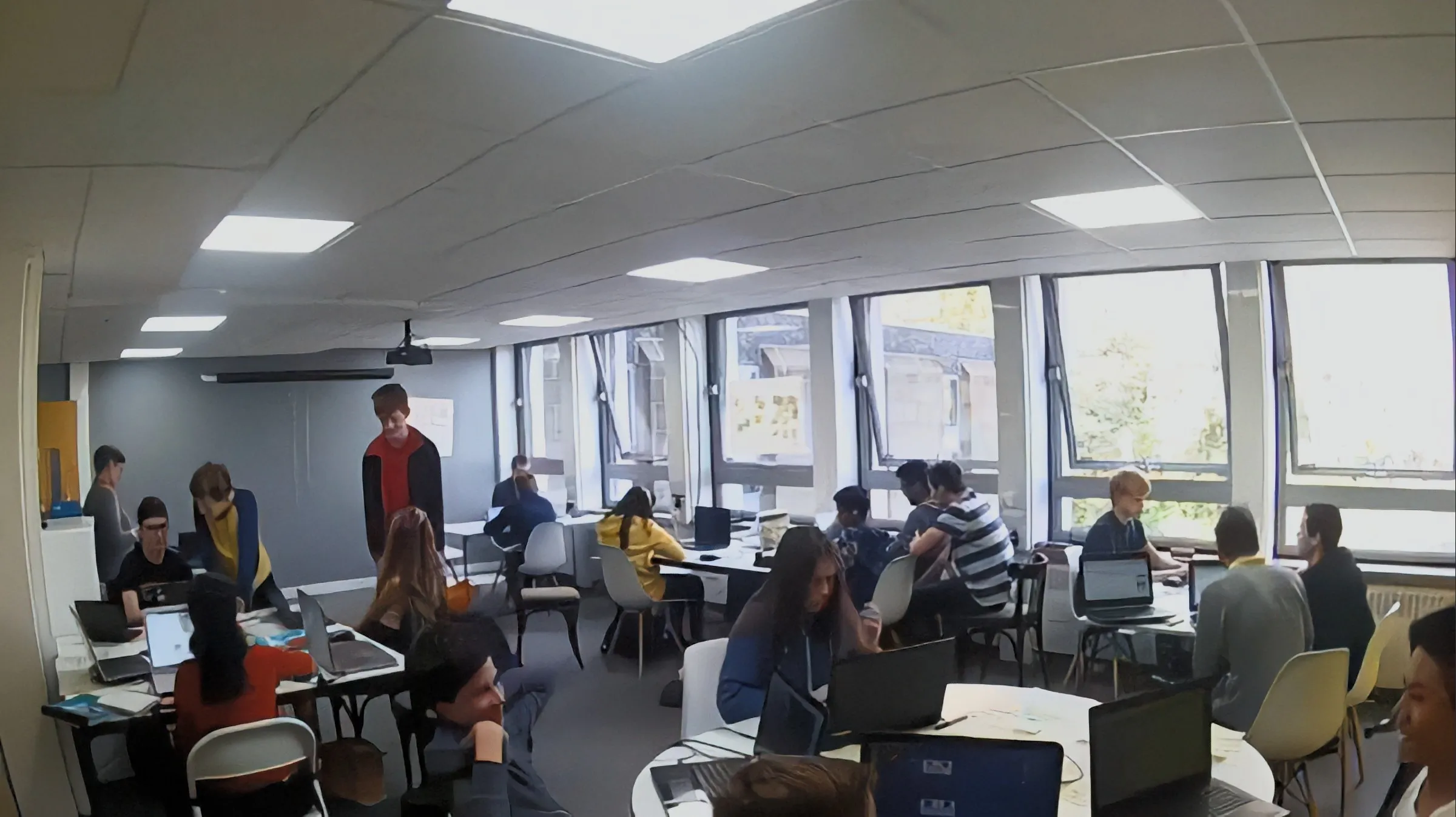 A still from a timelapse showing about 20 young people working on laptops at tables in a room