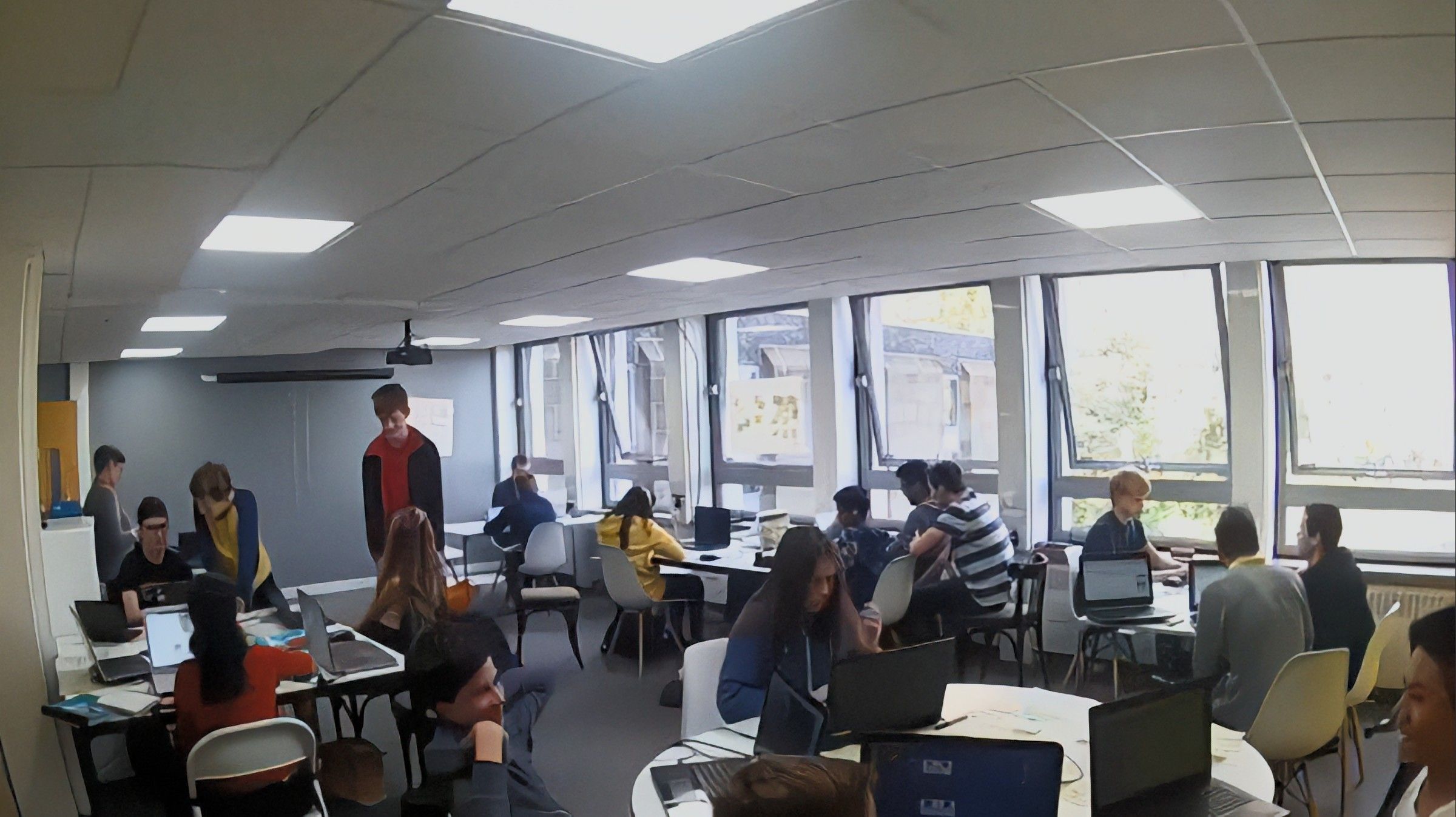 A still from a timelapse showing about 20 young people working on laptops at tables in a room