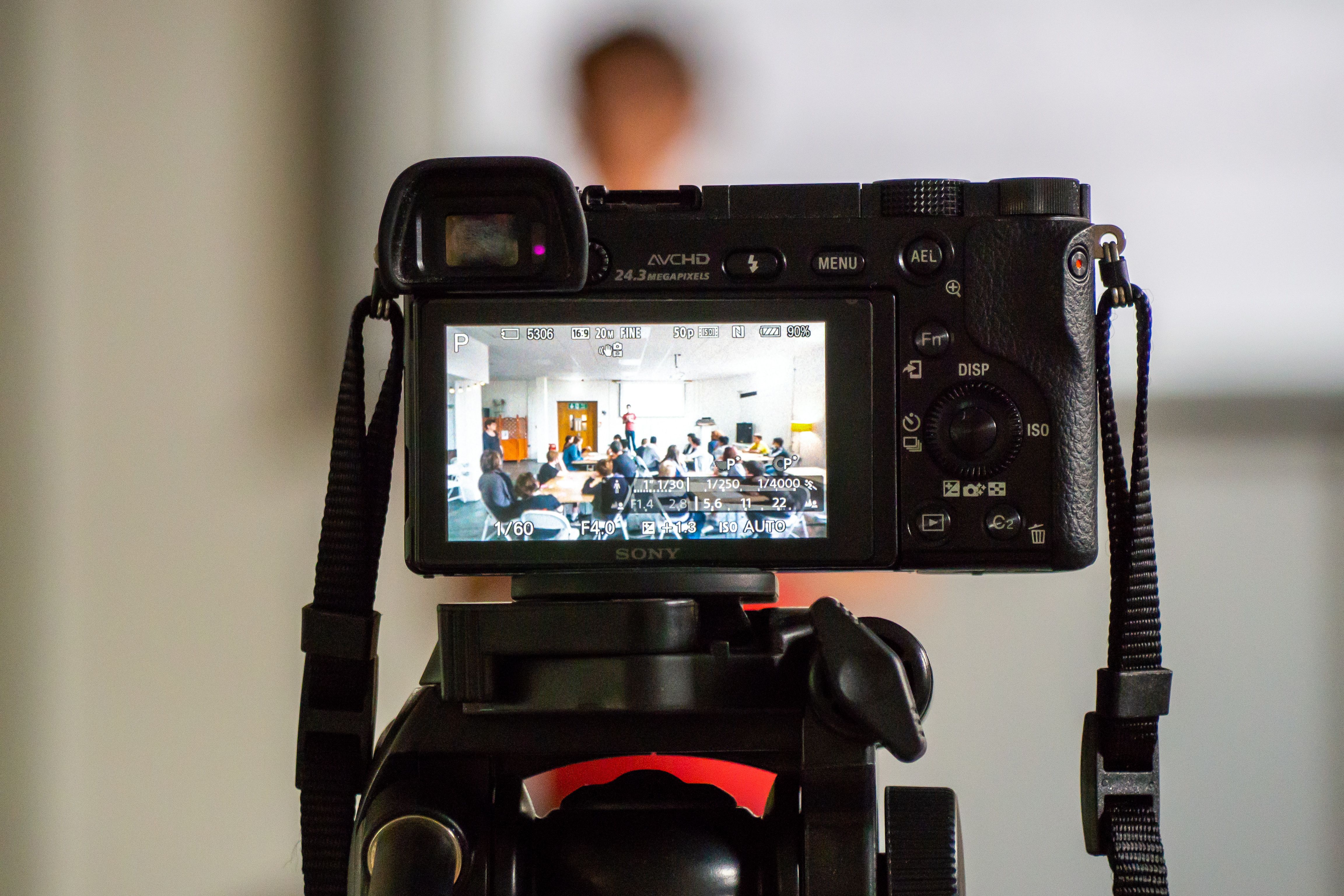 A camera pointed at a large room with young people working at tables