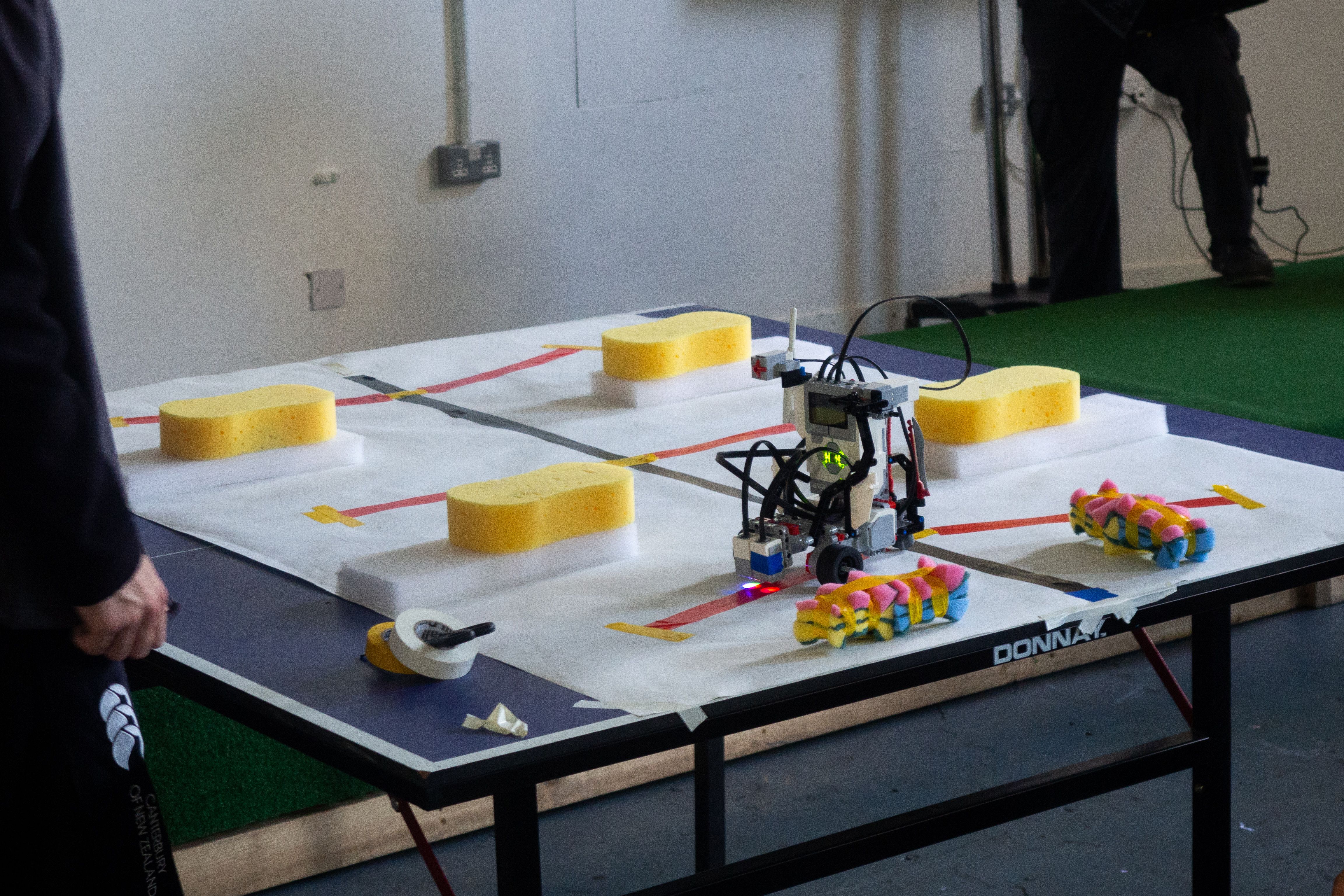 A LEGO robot standing in the middle of a makeshift obstacle course on a table