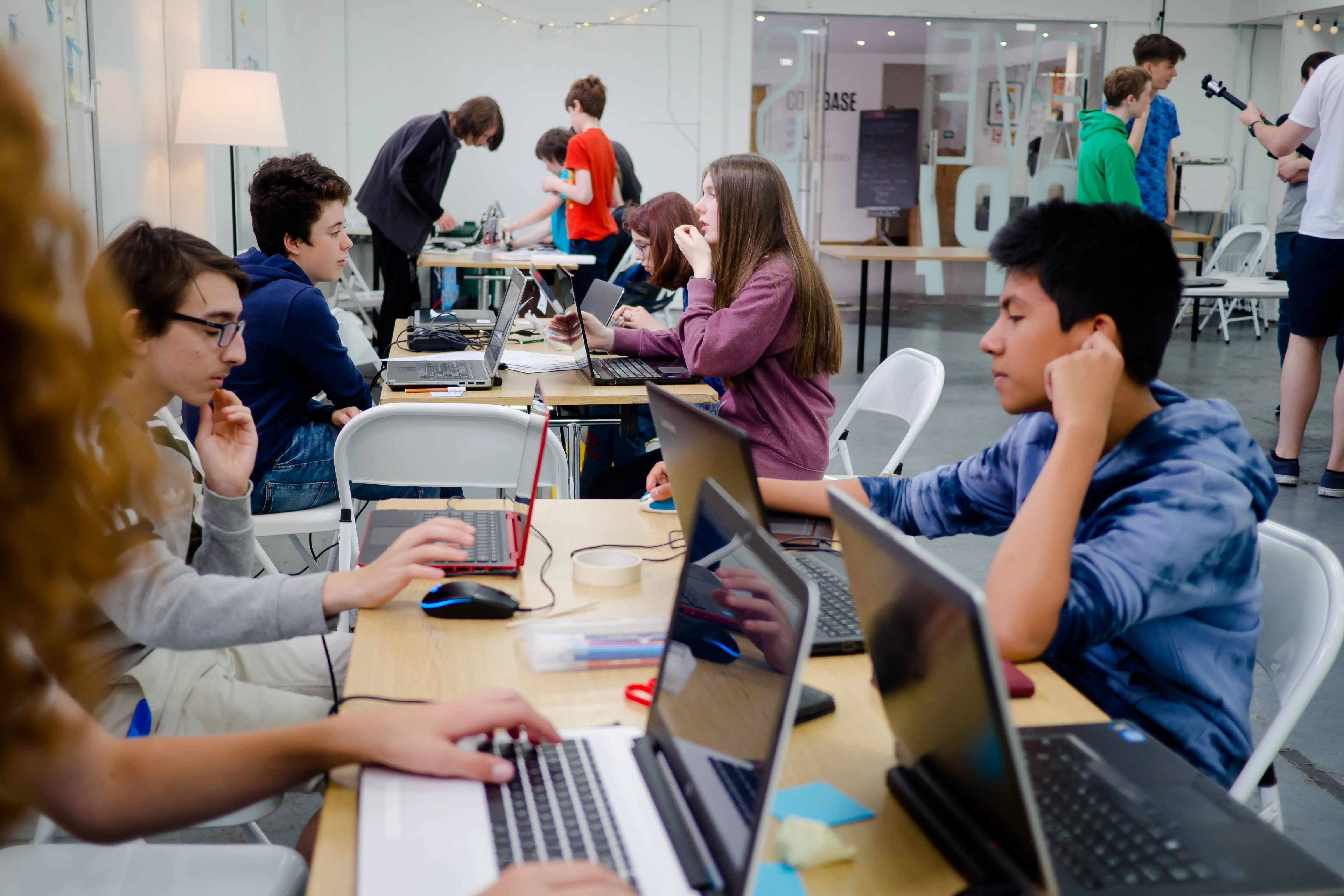 A few tables with 3-4 young people each working behind laptops