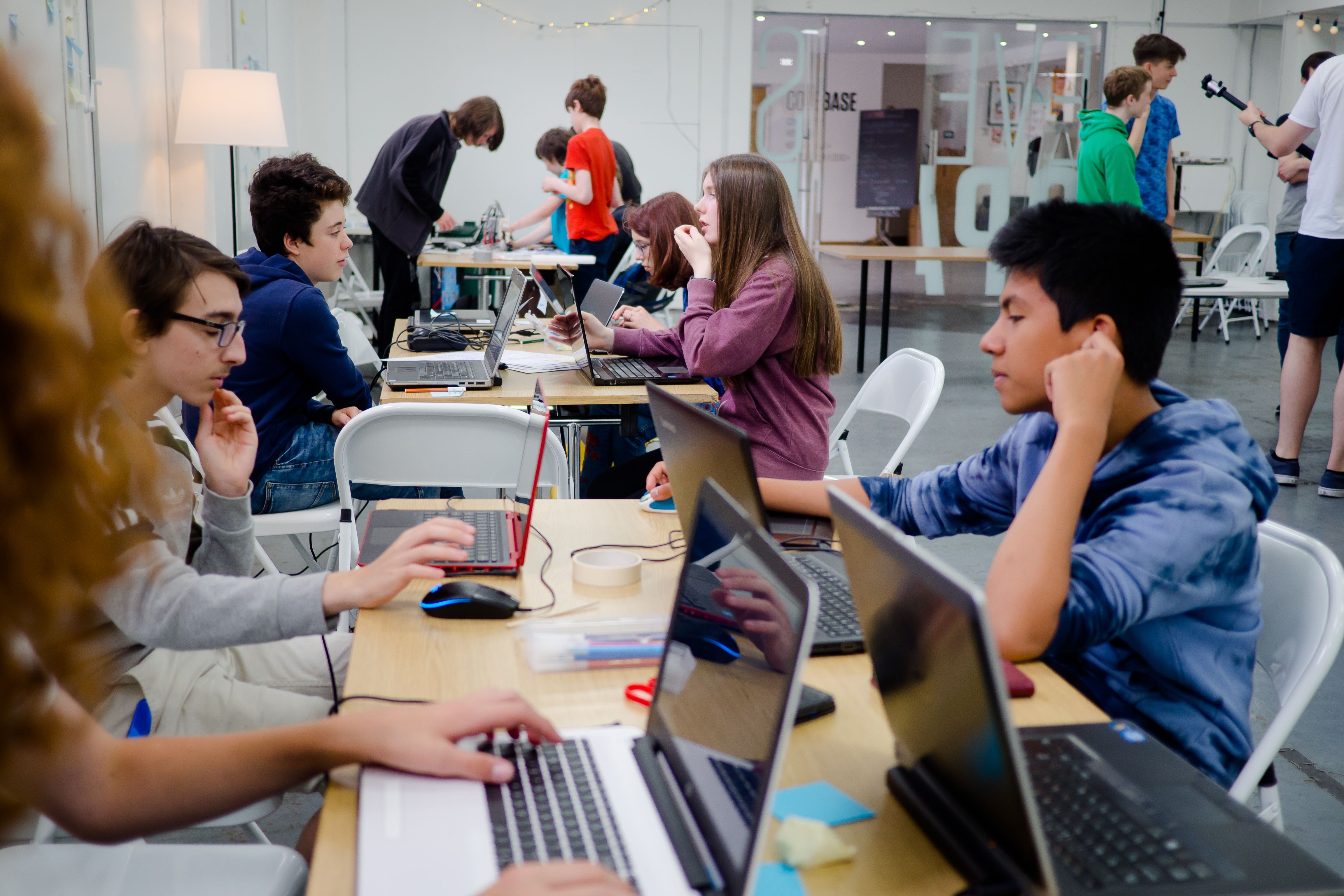 A few tables with 3-4 young people each working behind laptops