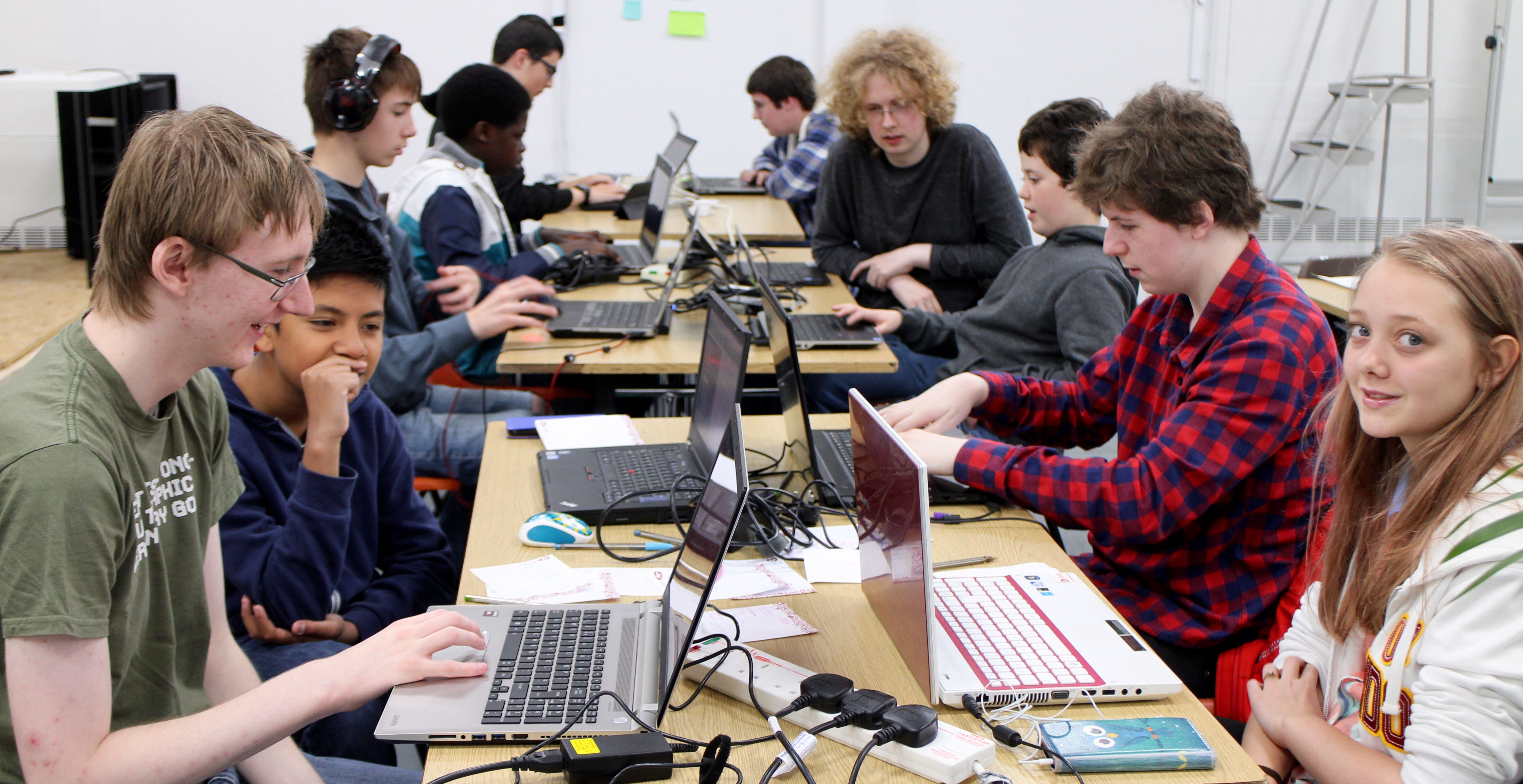 Young people working together on laptops at long tables