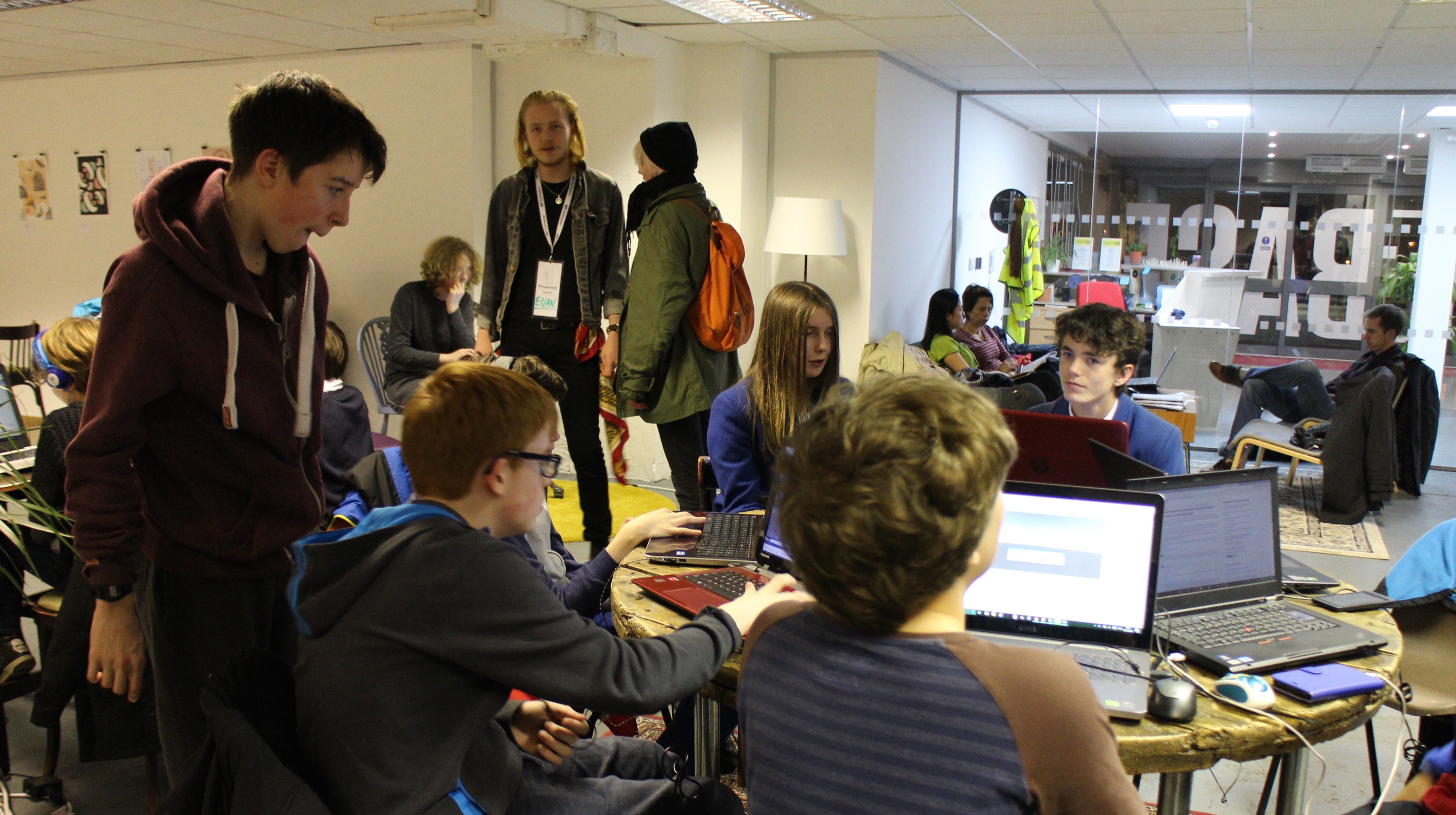 Young people working on laptops in the CodeBase coworking space with parents sitting in the background