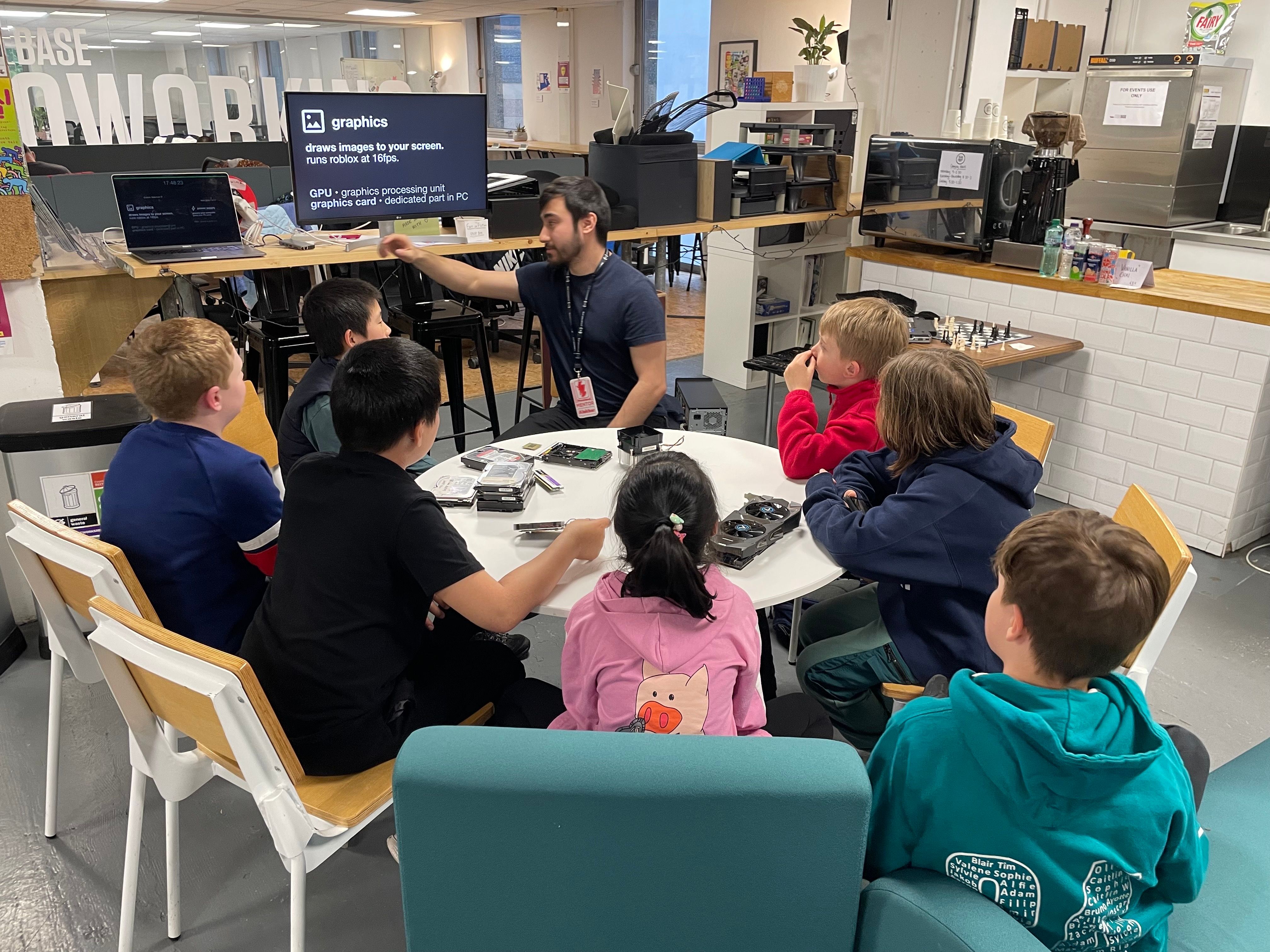 A Prewired mentor and 7 children sitting around a table with several PC components